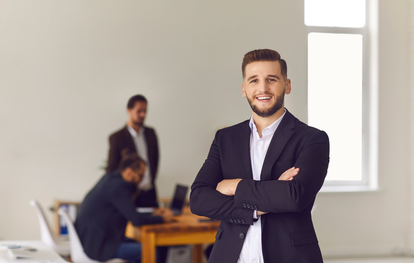 Smiling Office Worker or Businessman Looking at Camera with Colleagues Working at Background